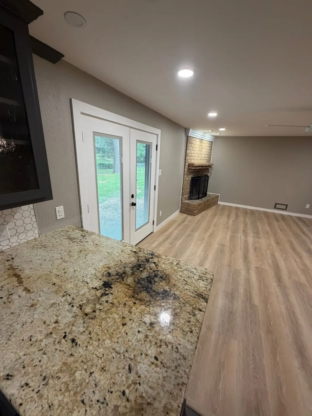 Granite peninsula overlooking new vinyl plank flooring and French doors
