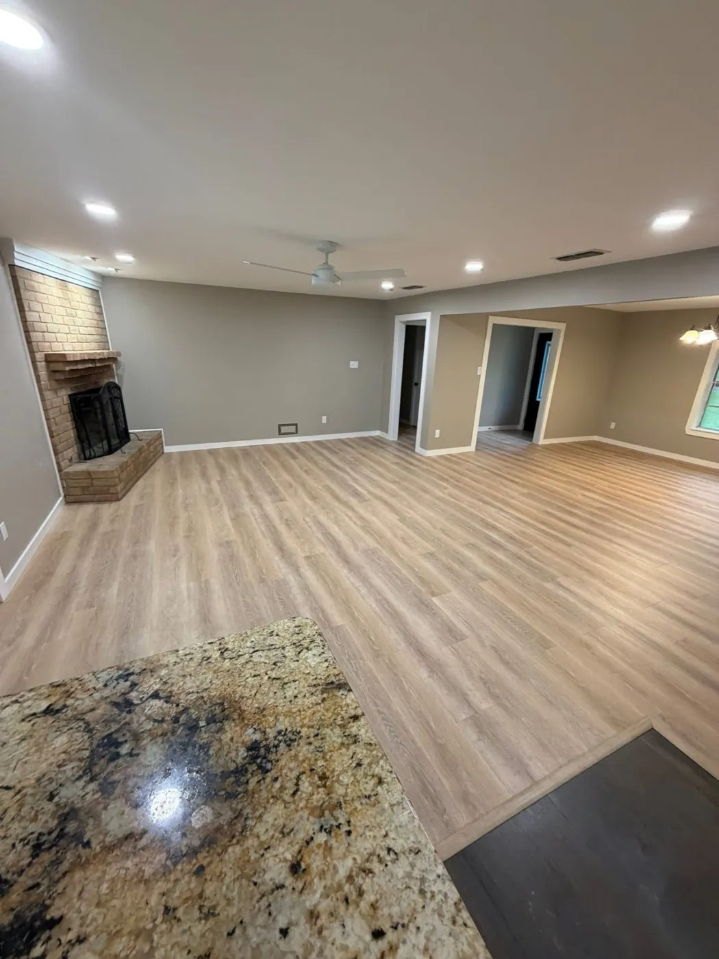Open living room with new wood-look flooring and brick fireplace