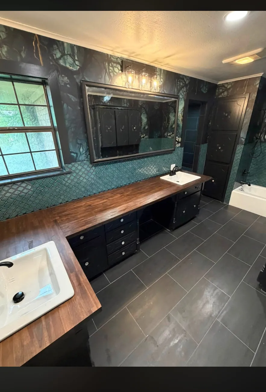 Master bathroom with forest-scene walls, teal tile backsplash, dark cabinets, and wood countertop